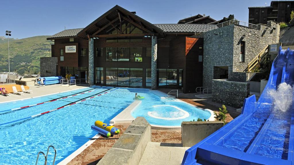 une piscine avec toboggan en face d'un bâtiment dans l'établissement APPART ZIG-ZAG LES COCHES, à Les Coches