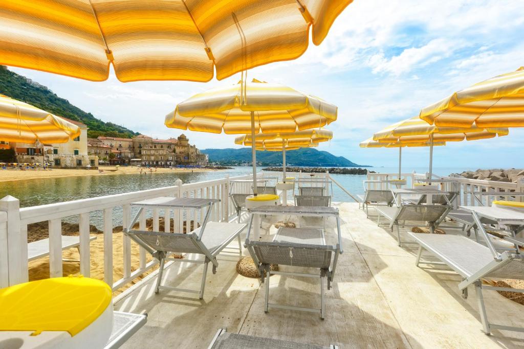 une terrasse avec des parasols jaunes, des tables et des chaises dans l'établissement Hotel La Marina, à Santa Maria di Castellabate
