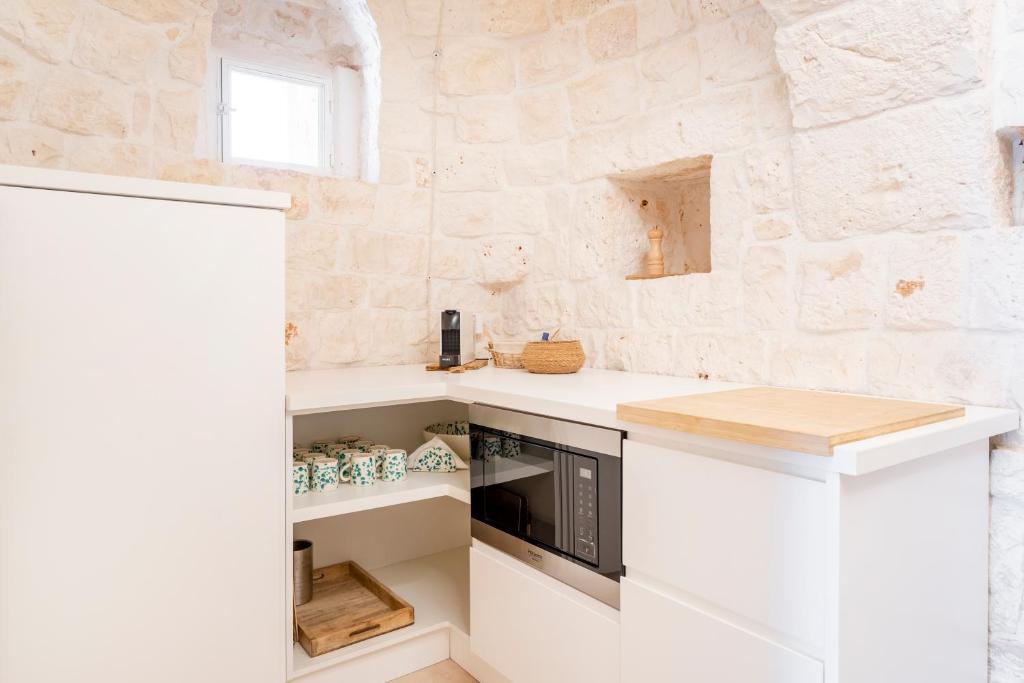 - une cuisine avec des placards blancs et un mur en pierre dans l'établissement Trulli Cicerali , trulli design con piscina panoramica, à Ostuni