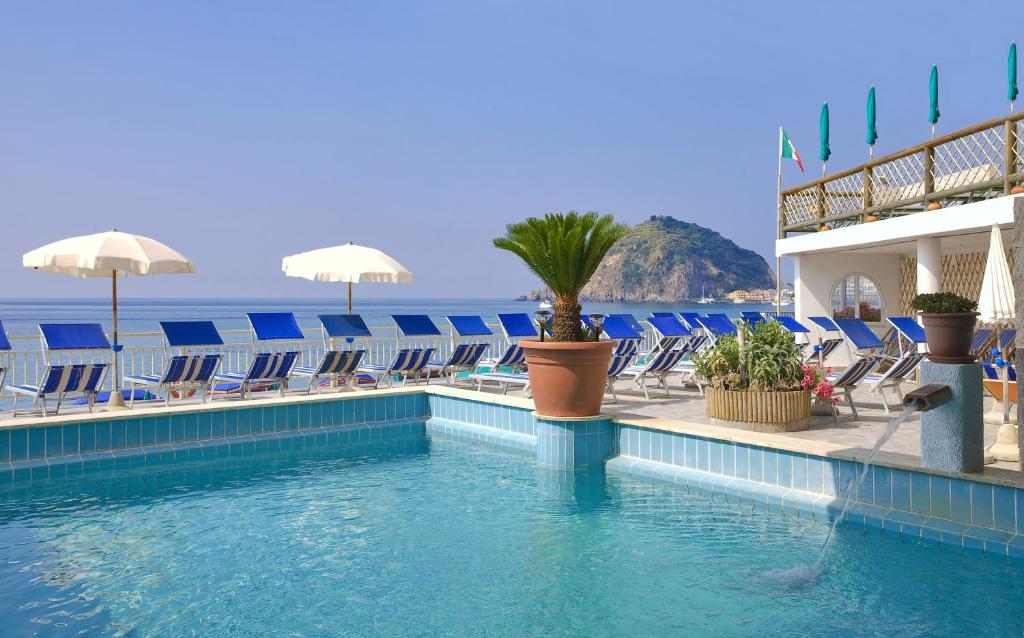 une piscine avec des chaises et l'océan en arrière-plan dans l'établissement Hotel Vittorio Beach Resort, à Ischia