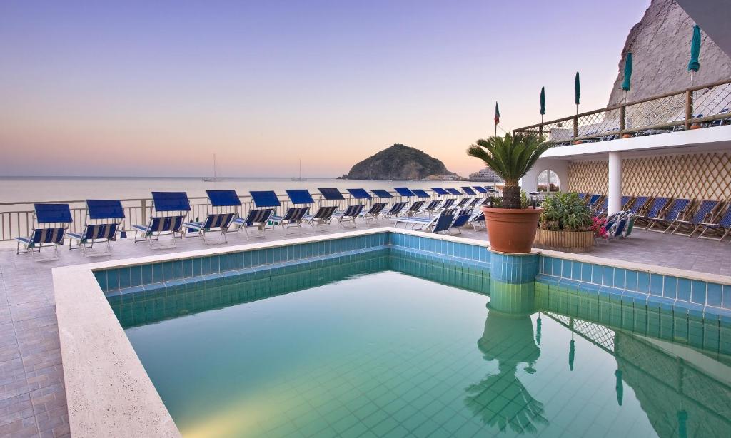 une piscine avec des chaises et l'océan en arrière-plan dans l'établissement Hotel Vittorio Beach Resort, à Ischia