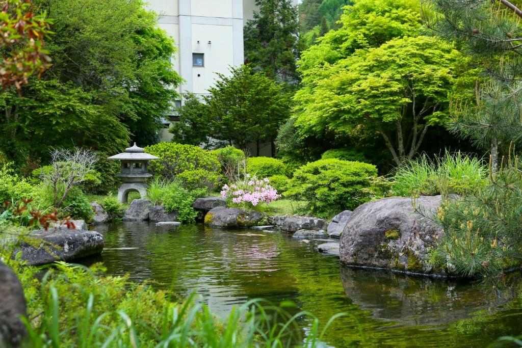 un jardin avec un étang, des rochers et des arbres dans l'établissement Ooedo Onsen Monogatari Shinshu Kakeyu, à Ueda