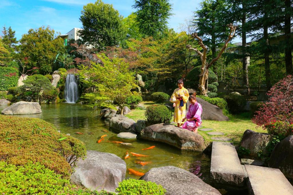 2 personnes debout sur des rochers près d'un étang avec une cascade dans l'établissement Ooedo Onsen Monogatari Hotel Shinko, à Fuefuki