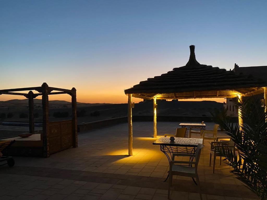 d'une terrasse avec des tables et un pavillon offrant une vue sur le coucher du soleil. dans l'établissement Hotel Riad Xaluca, à Merzouga
