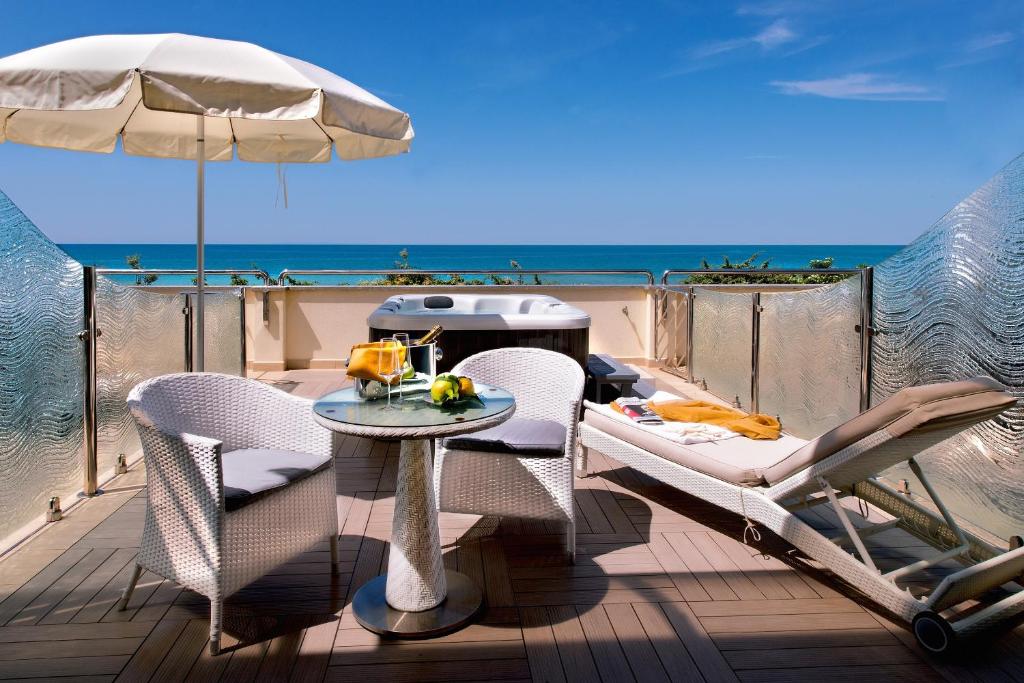une table et des chaises sur une terrasse avec un parasol dans l'établissement Hotel I Ginepri, à Marina di Castagneto Carducci
