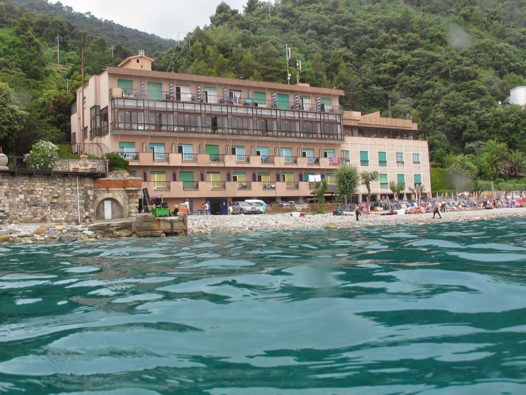 un bâtiment sur une plage à côté d'un plan d'eau dans l'établissement Hotel Capo Noli, à Noli