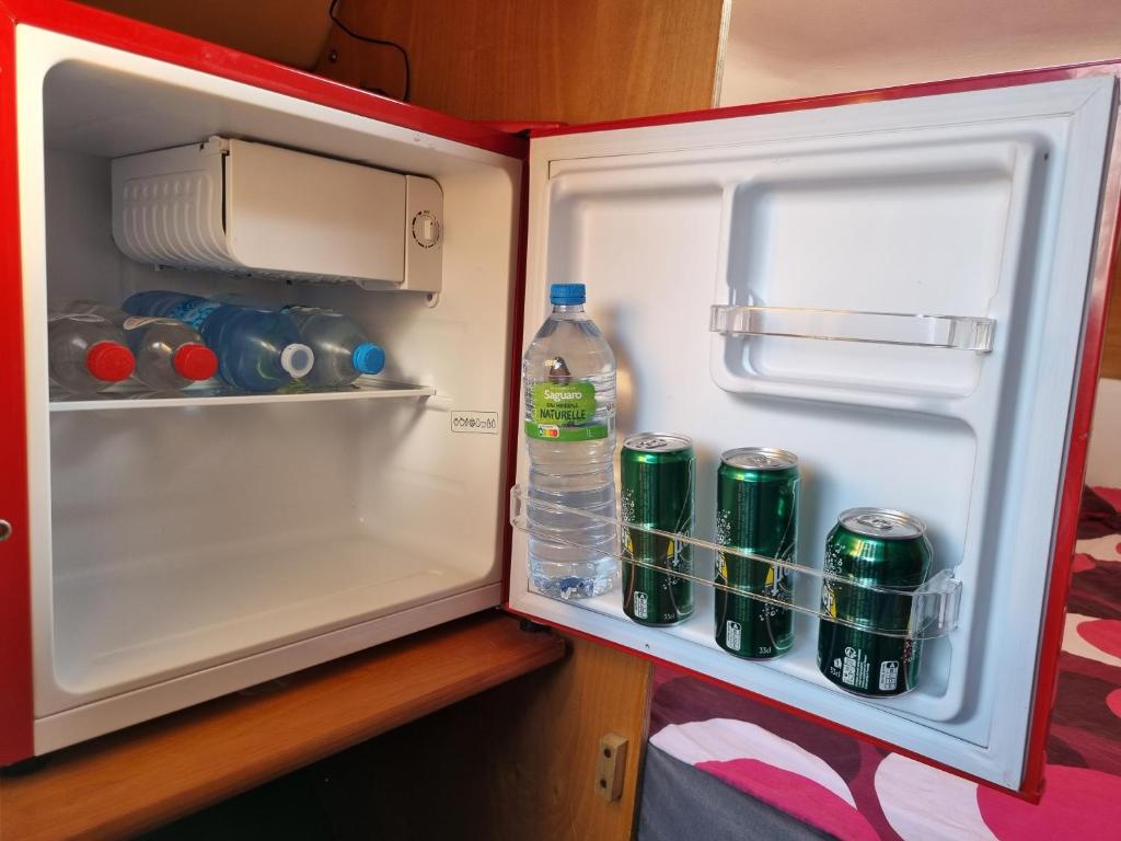 un réfrigérateur ouvert avec une bouteille d'eau et des canettes de soda dans l'établissement VOILIER AU SOLEIL LEVANT, au Havre