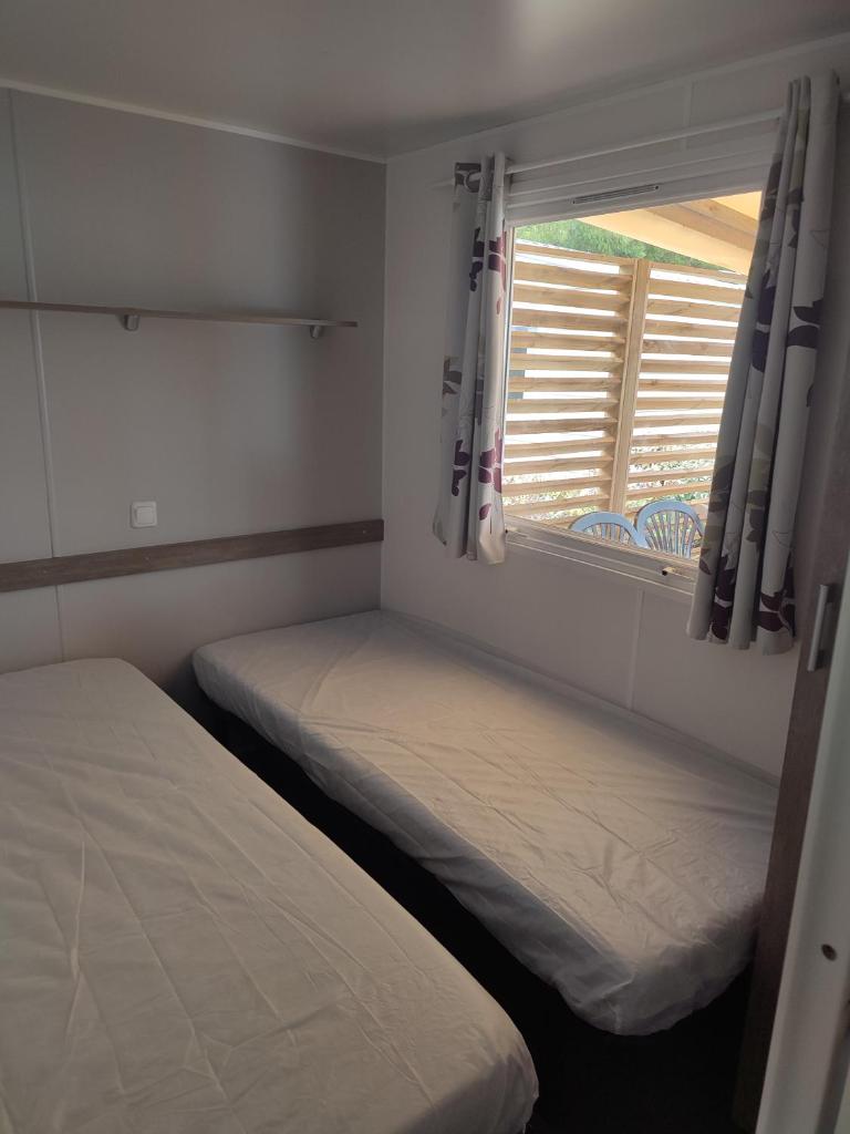 deux lits dans une petite pièce avec une fenêtre dans l'établissement Mobil home, à Port-la-Nouvelle