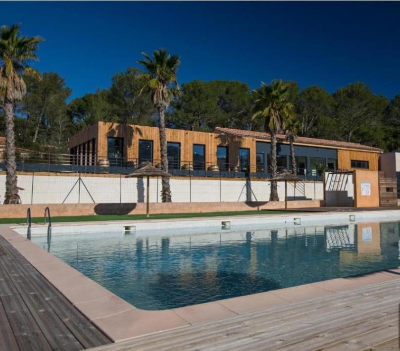 une piscine devant un immeuble avec des palmiers dans l'établissement LUXUEUX MOBIL-HOME, à Pierrefeu-du-Var