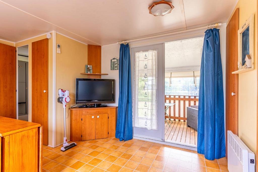 un salon avec des rideaux bleus et une télévision dans l'établissement Mobilhome bord de mer Gujan Mestras, à Gujan-Mestras