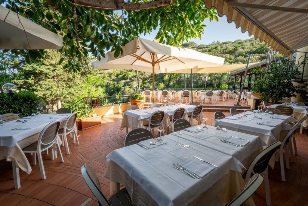 un restaurant avec des tables blanches, des chaises et des parasols dans l'établissement Hotel Anna, à Fetovaia