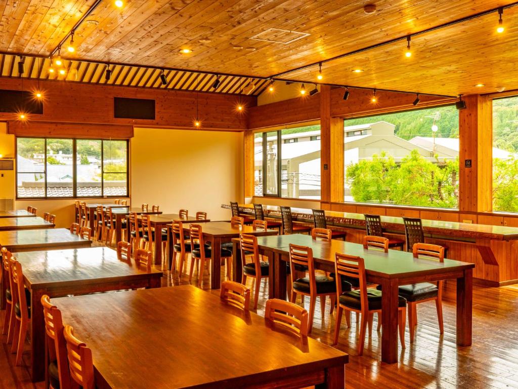un restaurant avec des tables et des chaises en bois et des fenêtres dans l'établissement Yawaragi-no-Sato Yadoya, à Yufu