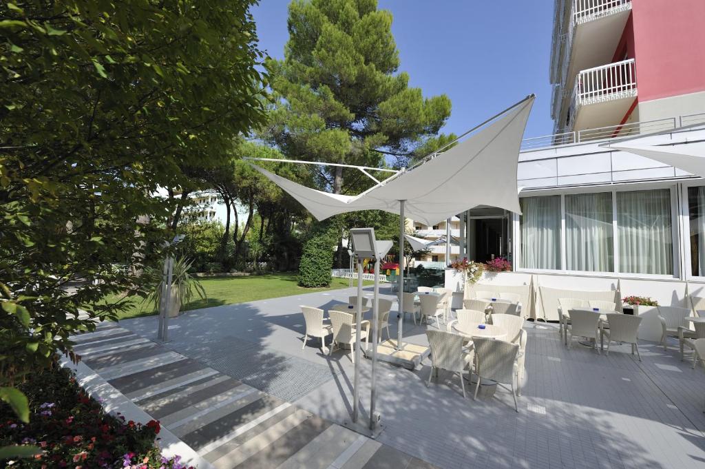 une terrasse avec des tables et des chaises blanches devant un bâtiment dans l'établissement Hotel Eden, à Bibione