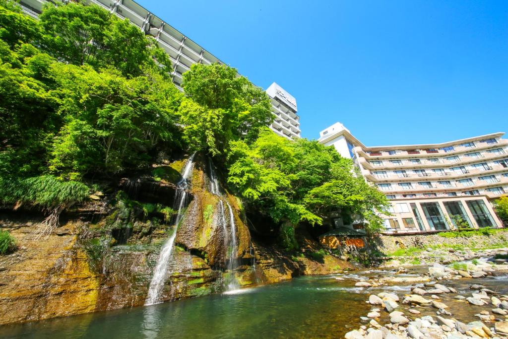 une cascade dans une rivière avec des bâtiments en arrière-plan dans l'établissement Ooedo Onsen Monogatari Premium Hotel New Shiobara, à Nasushiobara