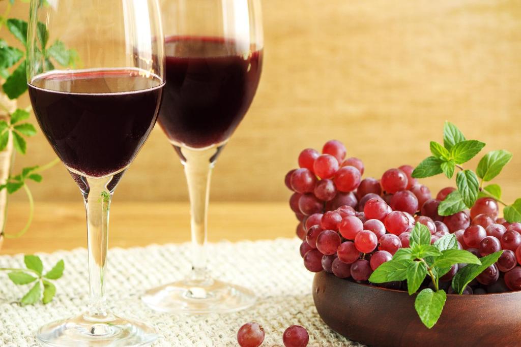 deux verres de vin rouge à côté d'un bol de raisins dans l'établissement ホテル南の風風力3駒ヶ根店, à Komagane
