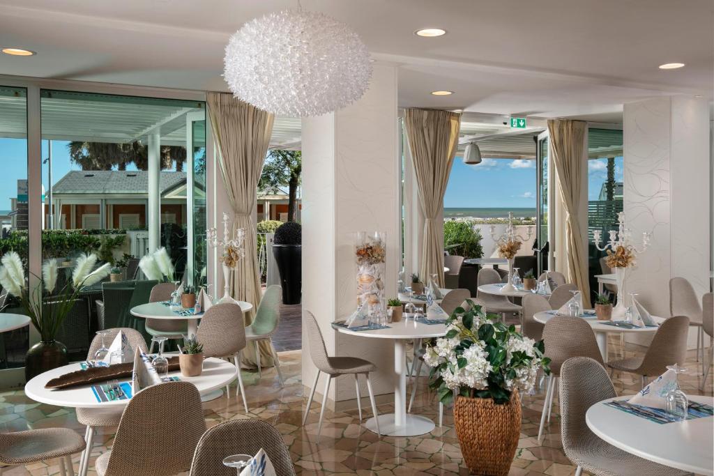 un restaurant avec des tables et des chaises blanches et des fenêtres dans l'établissement Hotel Ca' Bianca, à Riccione