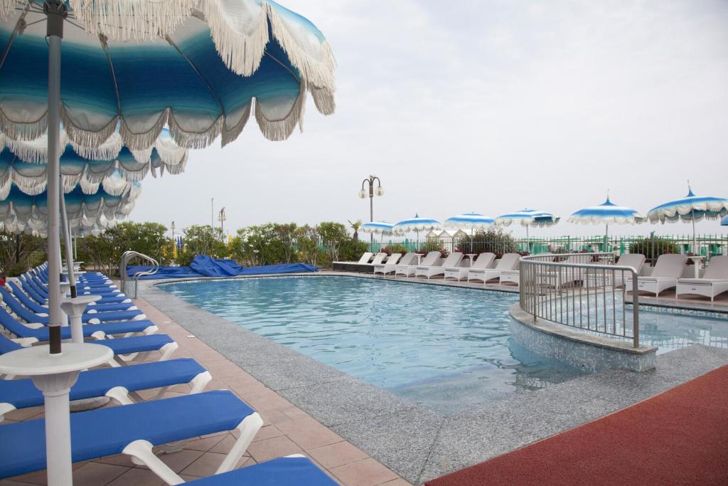 une piscine avec des chaises longues et un parasol dans l'établissement Hotel Elpiro, à Lido di Jesolo