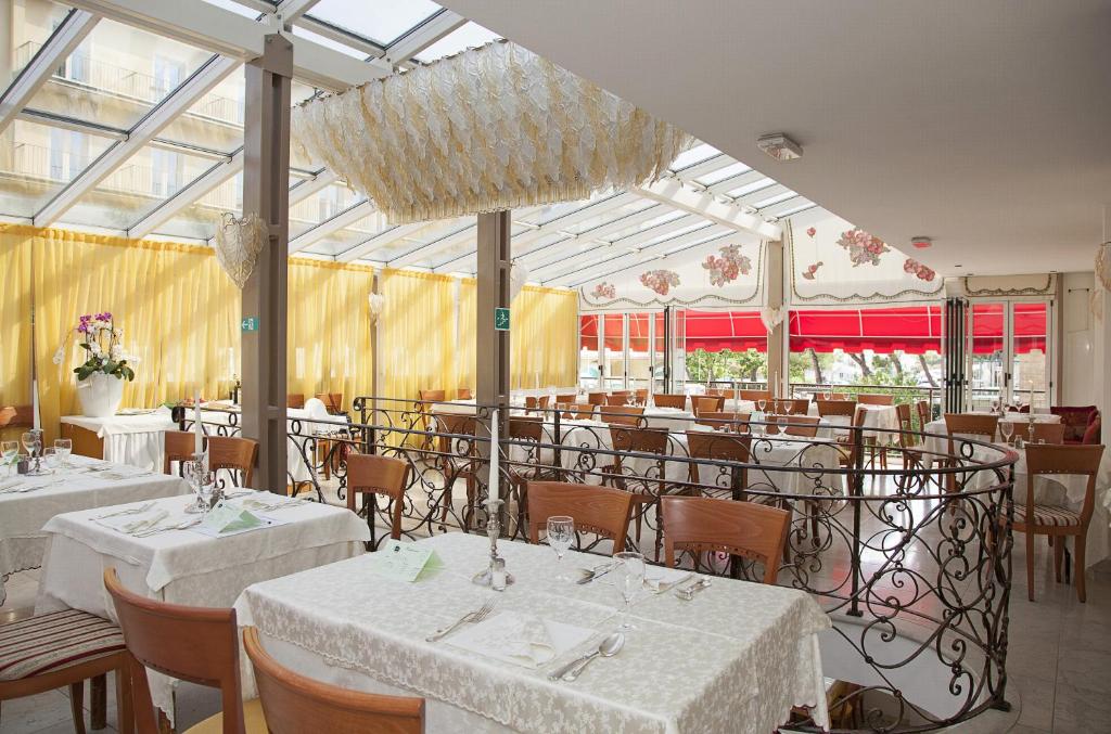 une salle à manger avec des tables et des chaises blanches et des fenêtres dans l'établissement Hotel Elpiro, à Lido di Jesolo