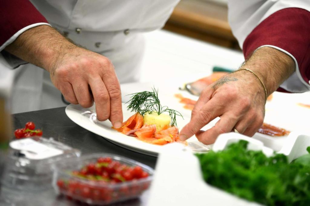 un chef préparant une assiette de nourriture sur un comptoir dans l'établissement Green Village Eco Resort, à Lignano Sabbiadoro 93 autres photos