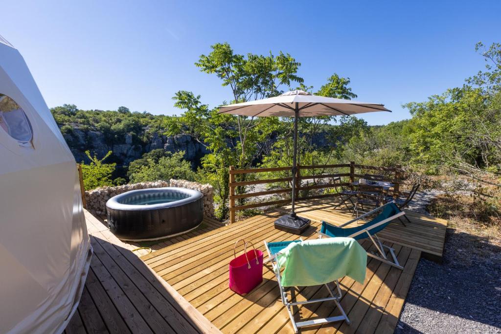 une terrasse avec un parasol et des chaises et un bain à remous dans l'établissement Les Dômes des Gorges, à Ruoms