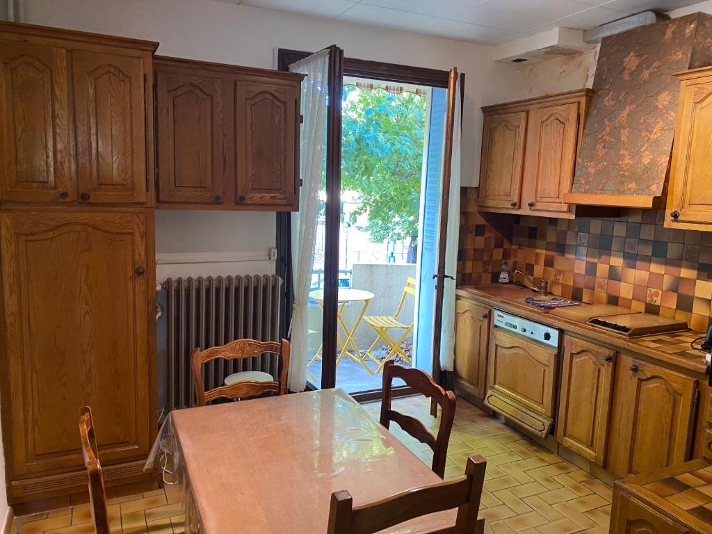 une cuisine avec des armoires en bois et une table avec des chaises dans l'établissement NOUVEAU Maison de la place, à Jaujac