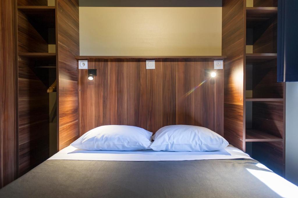 - un lit avec une tête de lit en bois et 2 oreillers blancs dans l'établissement Huttopia Les Châteaux, à Bracieux
