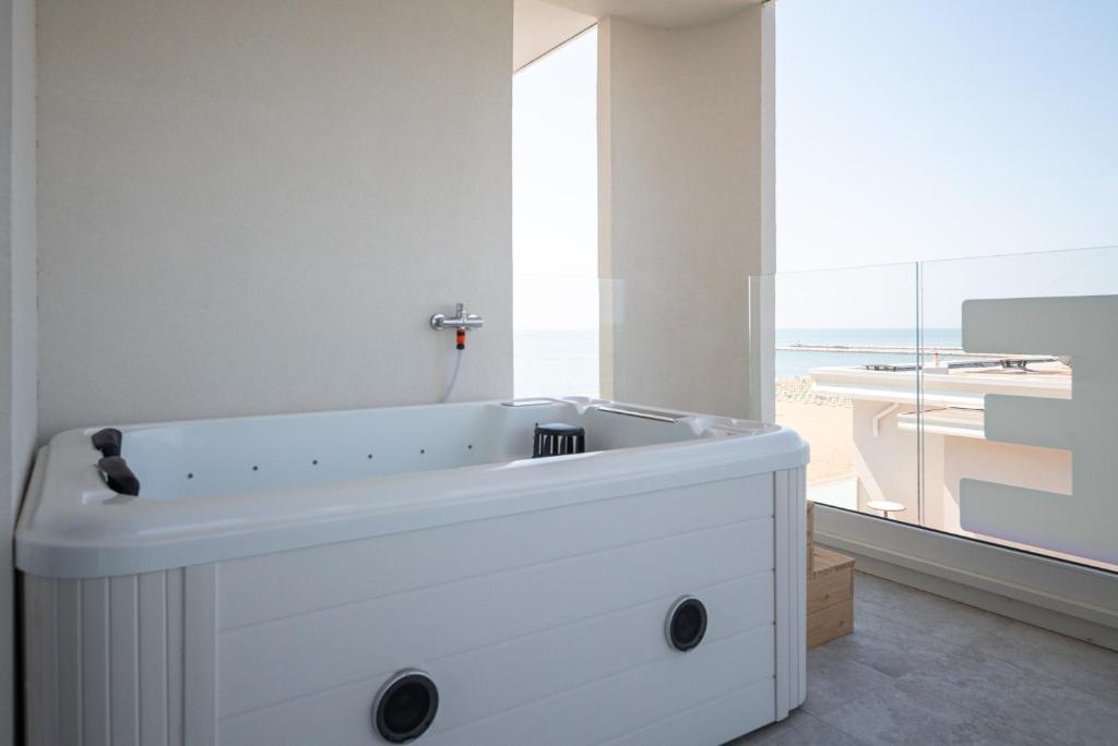 une baignoire blanche dans une salle de bains avec fenêtre dans l'établissement Unico Hotel Caorle, à Caorle