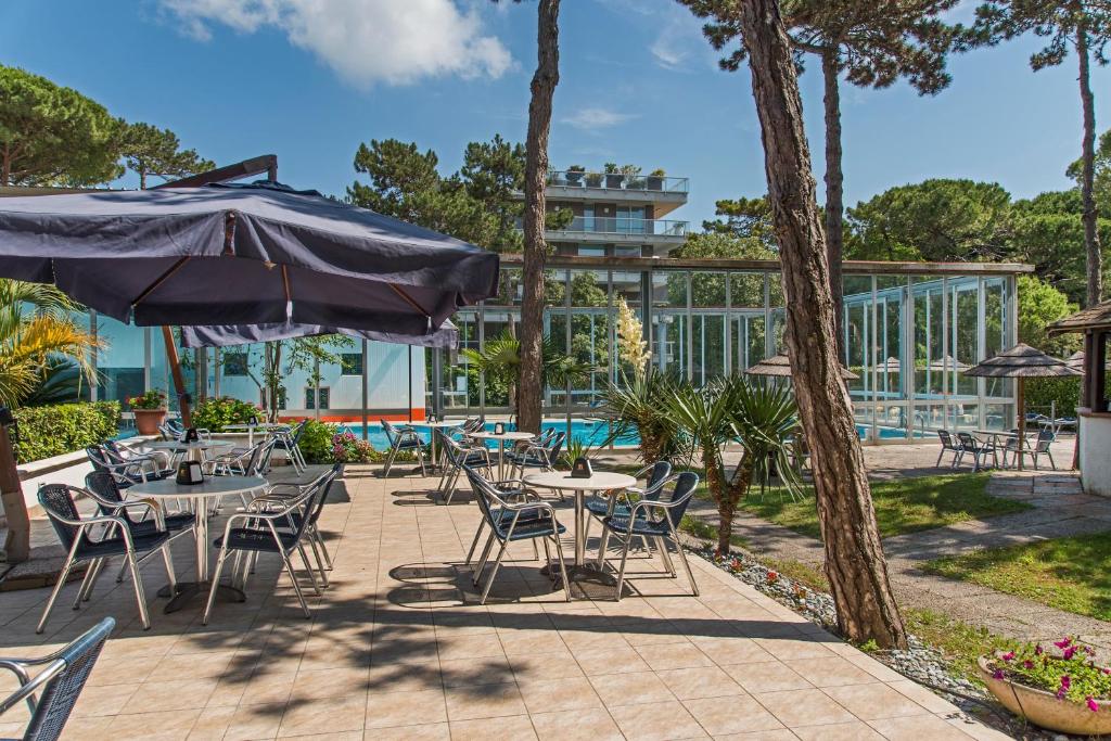 un patio avec tables, chaises et un parasol dans l'établissement Hotel Meridianus, à Lignano Sabbiadoro
