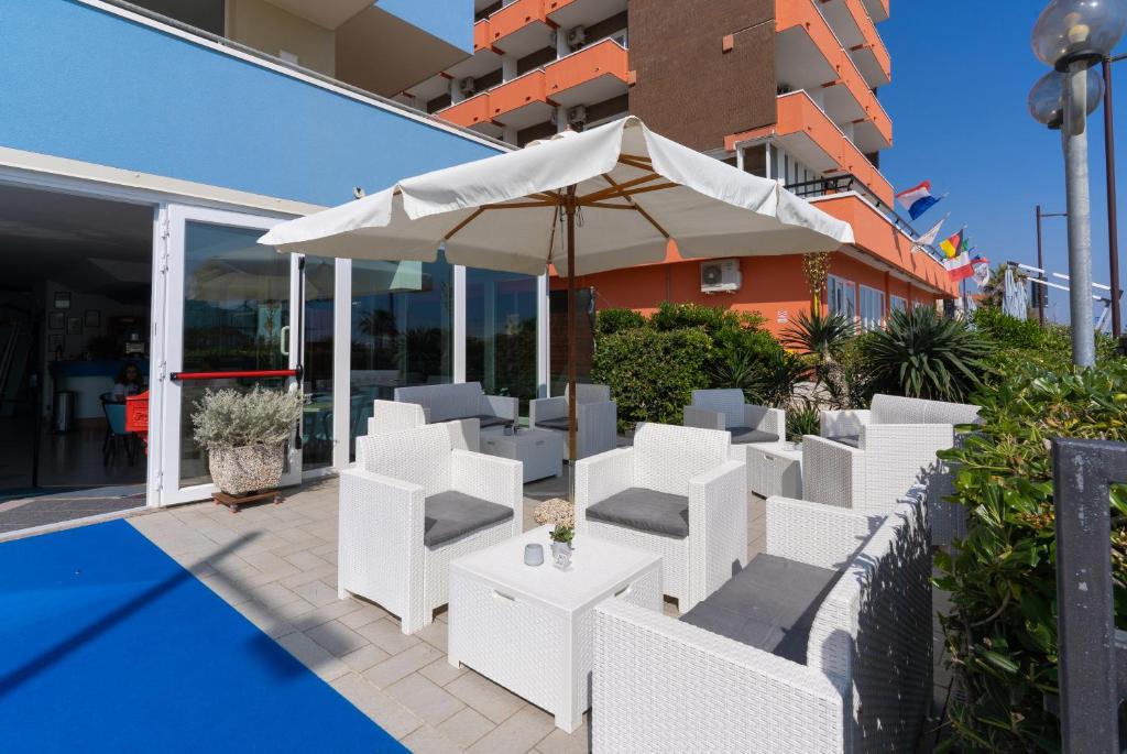 un patio avec des chaises blanches et un parasol dans l'établissement Hotel Croce Del Sud, à Rimini