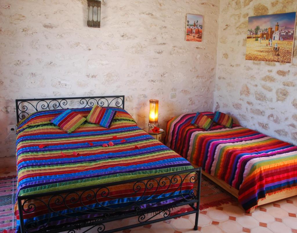- une chambre avec 2 lits avec des couvertures colorées et une lampe dans l'établissement Riad Titima Essaouira, à Essaouira