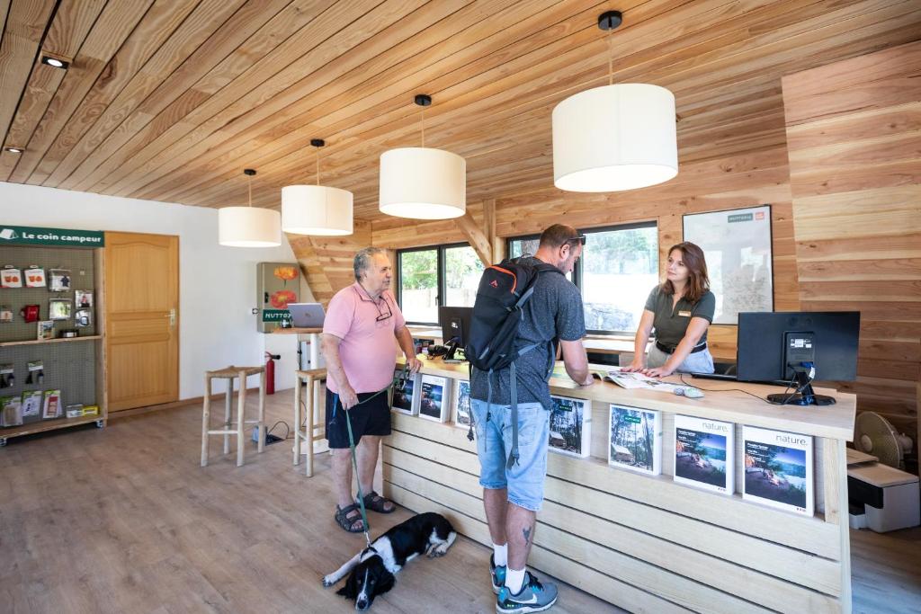 deux hommes et un chien debout à un comptoir dans l'établissement Huttopia Lac de Serre-Ponçon, à Le Lautaret