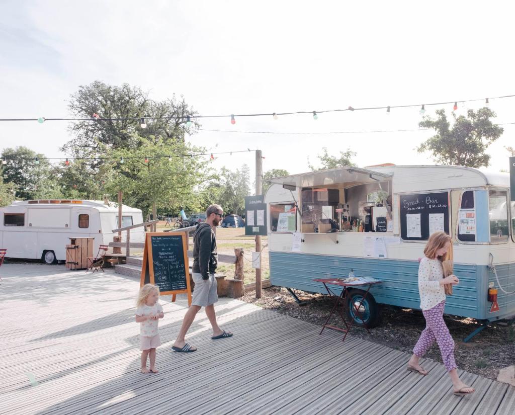 un homme, une femme et un enfant passant devant un food truck dans l'établissement Huttopia Calvados - Normandie, à Moyaux