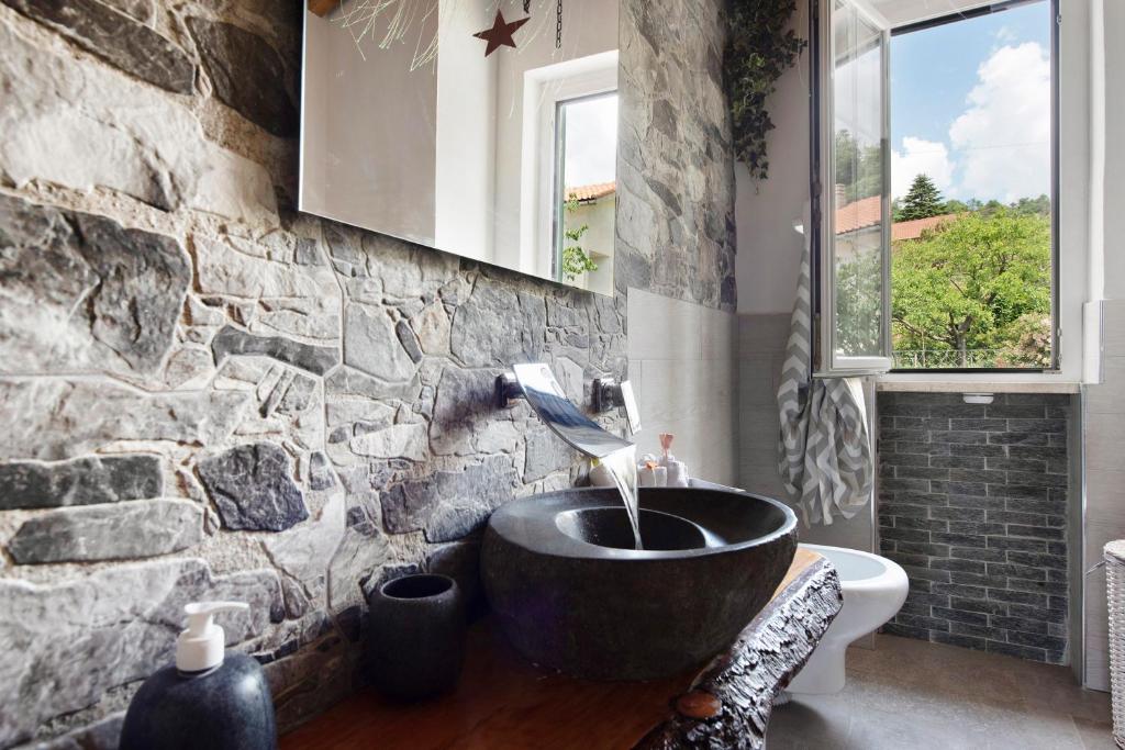 La salle de bains est pourvue d'un lavabo et d'un mur en pierre. dans l'établissement Barcollo House - Piscina nel verde, à Stella