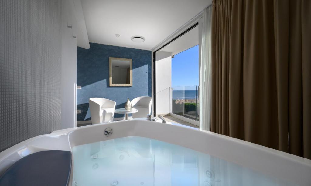une baignoire dans une salle de bain avec une grande fenêtre dans l'établissement Grand Hotel Playa, à Lignano Sabbiadoro