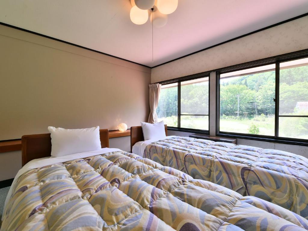 deux lits dans une chambre avec deux fenêtres dans l'établissement Alpine Route Hotel, à Omachi