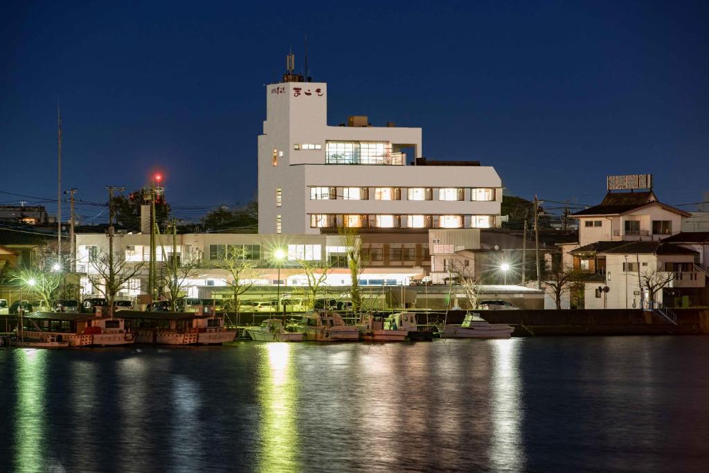 un grand bâtiment avec des bateaux dans l'eau la nuit dans l'établissement Hotel Shin Makomo, à Itako