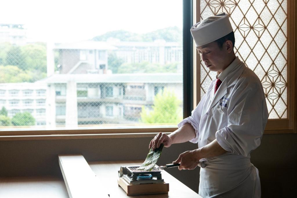 Un homme dans un chapeau préparant la nourriture sur une table dans l'établissement Arima Onsen ShikinoIrodori Hatago, à Kobe