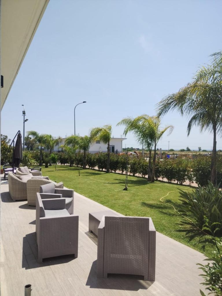 une rangée de chaises en osier et un parc avec des palmiers dans l'établissement Sand Hotel, à Botricello