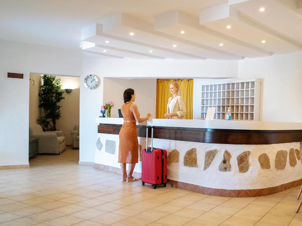 une femme avec une valise debout à un comptoir dans un hôtel dans l'établissement Hotel Pedra Santa, à Baja Sardinia 51 autres photos