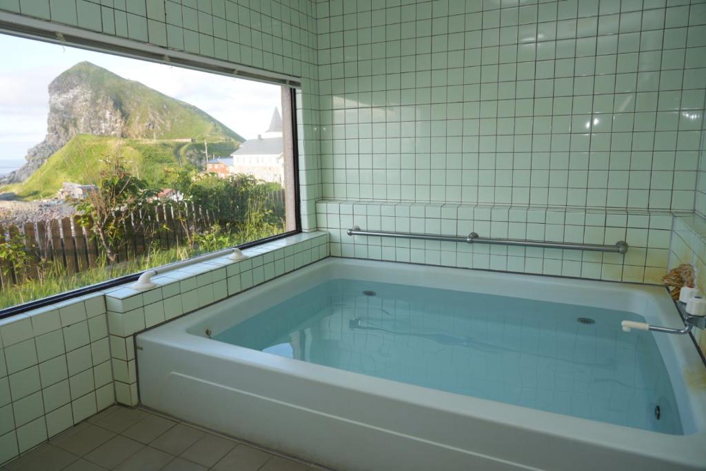 une baignoire dans une salle de bain carrelée avec une fenêtre dans l'établissement Shimanoyado Kamuirishiri, à Rishirifuji