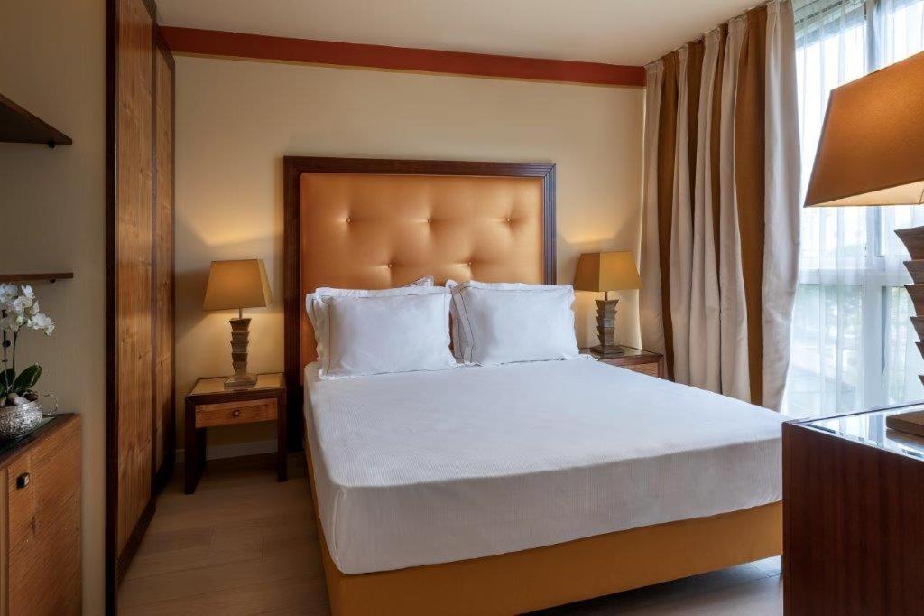 une chambre avec un grand lit avec des draps et des oreillers blancs dans l'établissement Hotel Greif, à Lignano Sabbiadoro