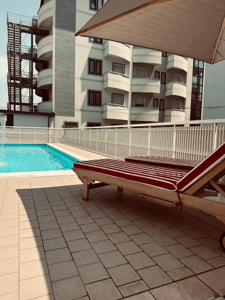 un banc à côté d'une piscine avec un bâtiment dans l'établissement MARITTIMO Milano Marittima, à Milano Marittima
