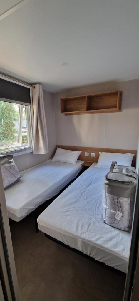 deux lits dans une petite pièce avec une fenêtre dans l'établissement Mobilhome 6P Camping la Carabasse Vias, à Vias