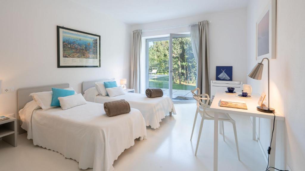 Cette chambre blanche dispose de deux lits, d'un bureau et d'une fenêtre. dans l'établissement Villa Giomoa 8, Emma Villas, à Capoliveri