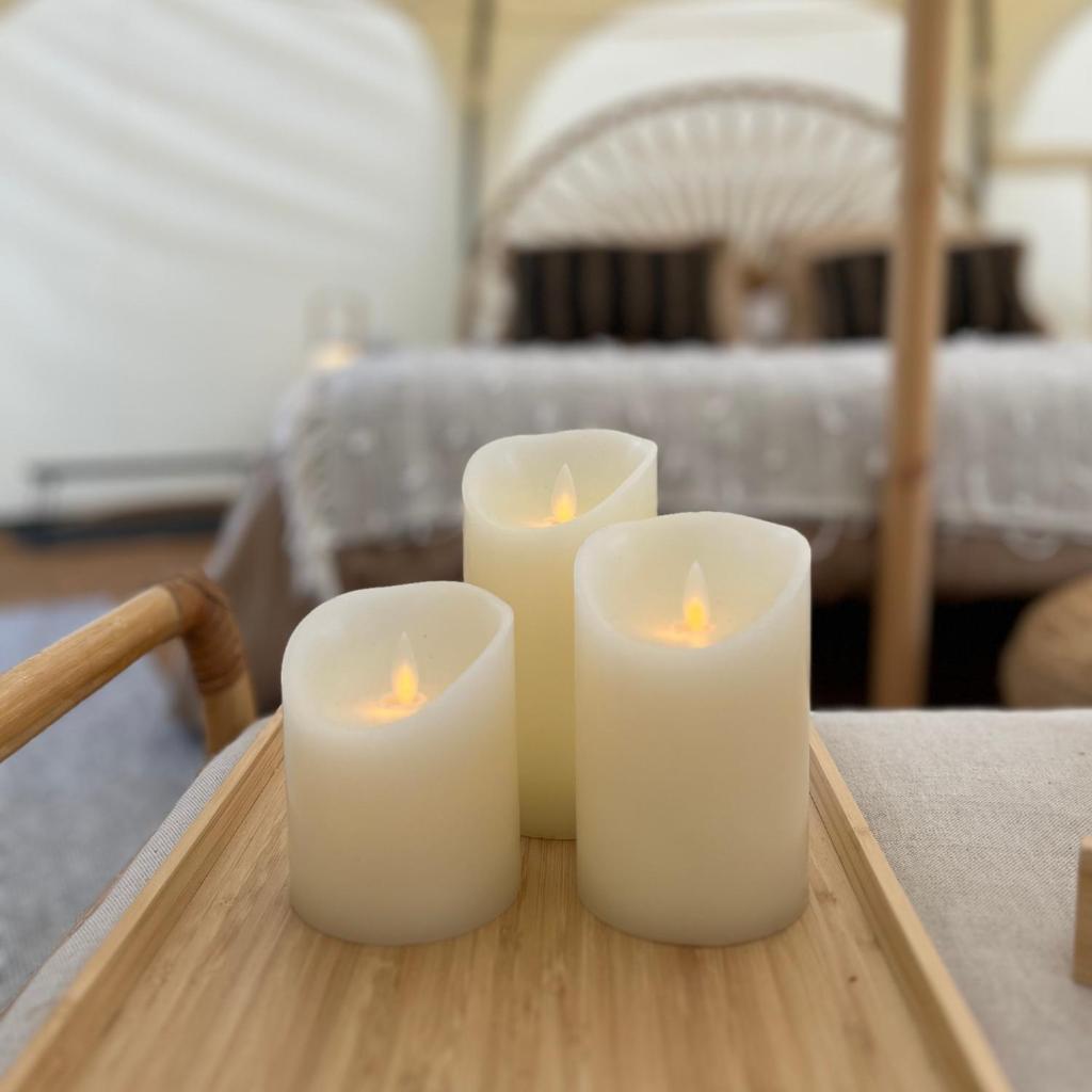 3 bougies blanches assises sur une table en bois dans l'établissement La Prairie Étoilée Luxury Glamping - Adults Only, à Crozon-sur-Vauvre