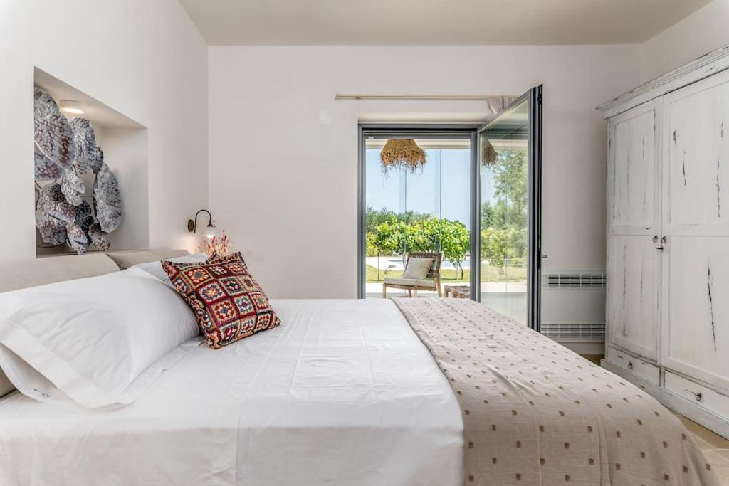 - une chambre blanche avec un grand lit et une porte coulissante en verre dans l'établissement LaCorte di Ninetta., à Ostuni
