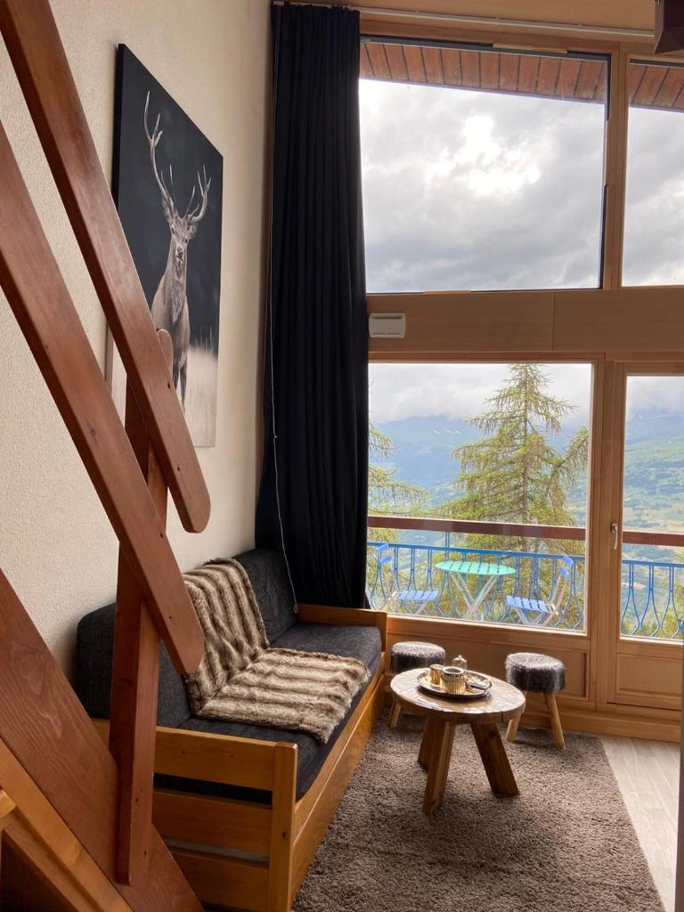 un salon avec un escalier et une grande fenêtre dans l'établissement RESIDENCE LE RUITOR Duplex dernier étage vue panoramique piscine chauffée en été classé 4 Cristaux Paradiski, à Arc 1800