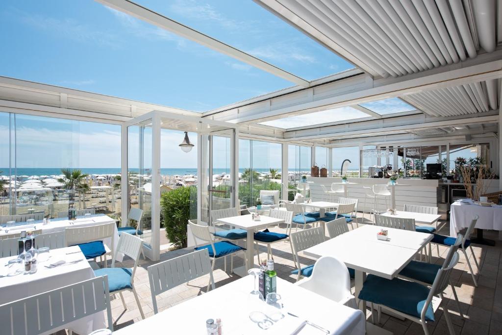 - un restaurant avec des tables et des chaises blanches et une vue sur l'océan dans l'établissement Hotel Astoria, à Caorle