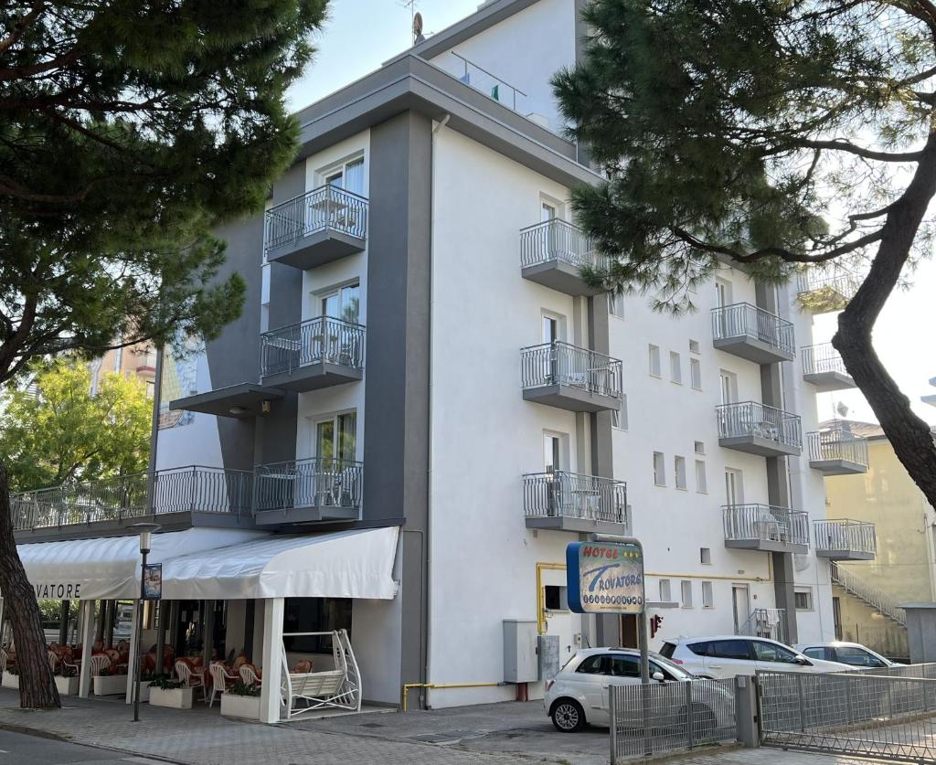 un bâtiment blanc avec des balcons et une voiture garée devant dans l'établissement Hotel Trovatore, à Lido di Jesolo