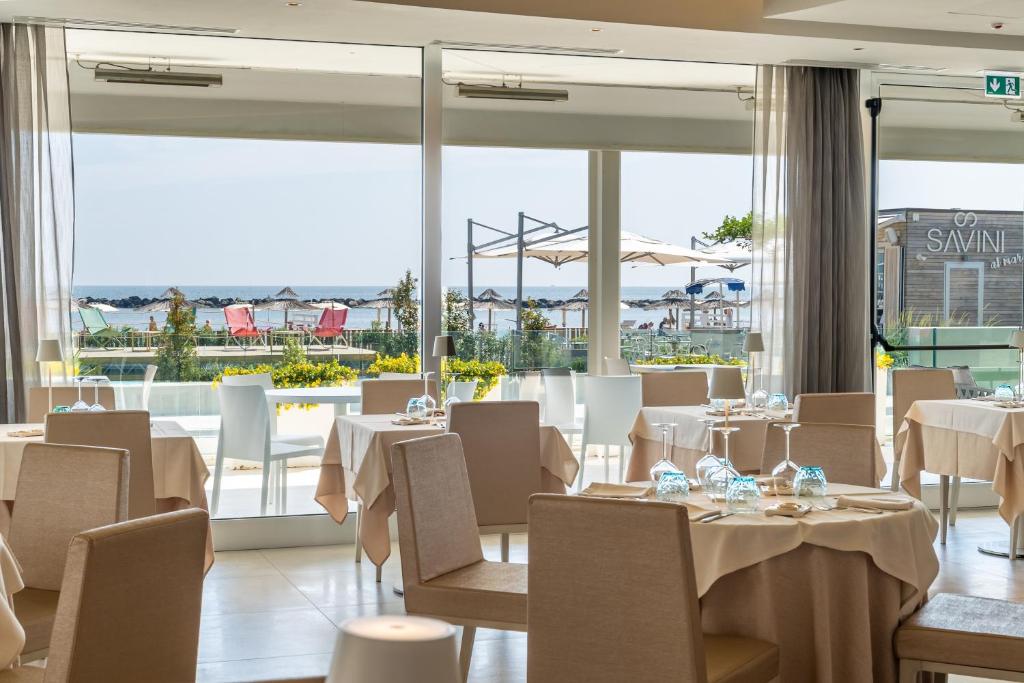 un restaurant avec des tables et des chaises blanches et de grandes fenêtres dans l'établissement Hotel Savini, à Bellaria-Igea Marina